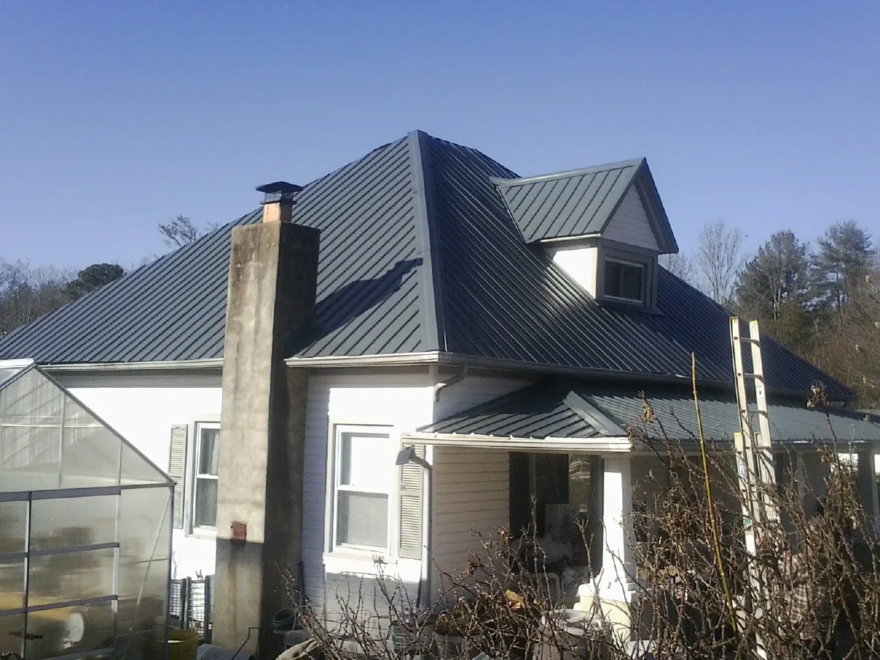 Dark blue standing seam metal roof on a white farmhouse with dormer — Slate & Tile Roof Repair by Roofing Brothers in Verndale