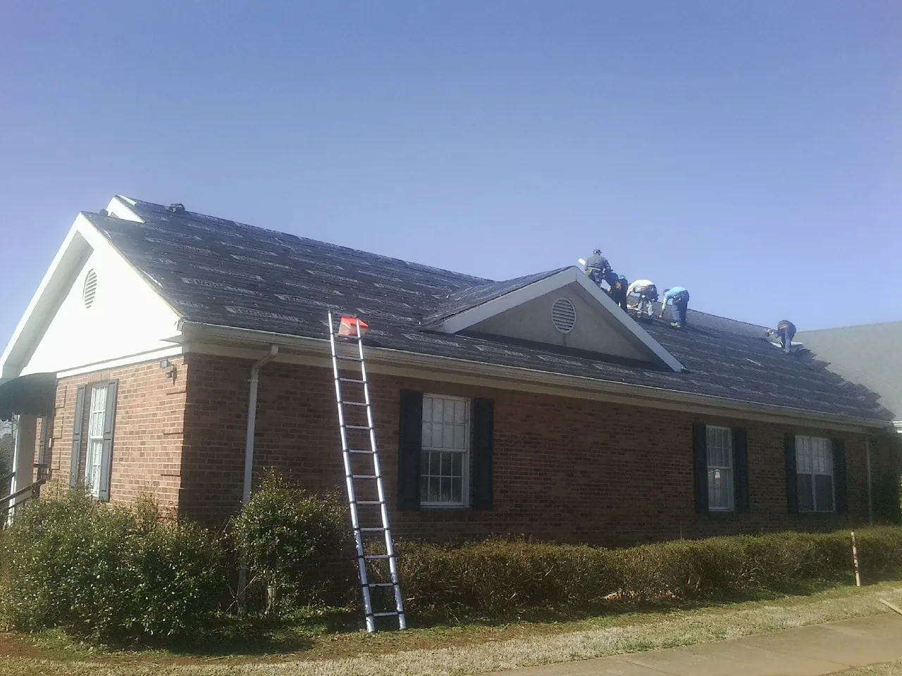 Crew tearing shingles off a brick ranch roof with a ladder set — Emergency Roof Repair work by our crew in Verndale