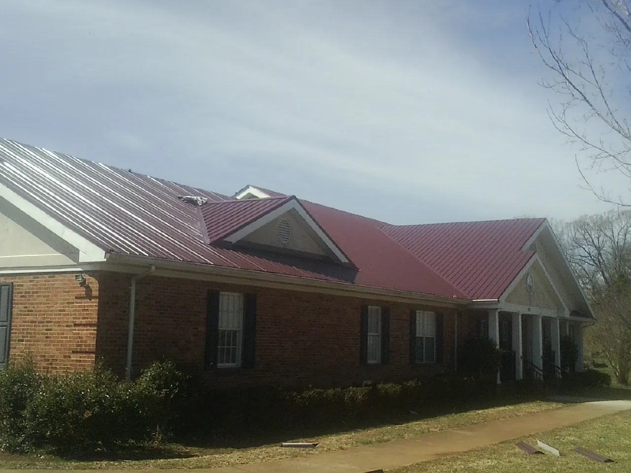 Red metal roof with gabled entries on a long brick building, from a Hail Damage Roof Repair job in Verndale