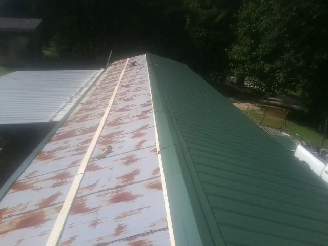 Old rusted panels beside newly installed green metal roofing — Wind Damage Roof Repair by Roofing Brothers in Verndale