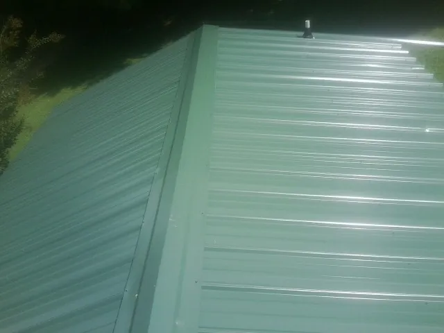 New green metal panels meeting at the ridge of a roof — Flat Roof Repair work by our crew in Verndale