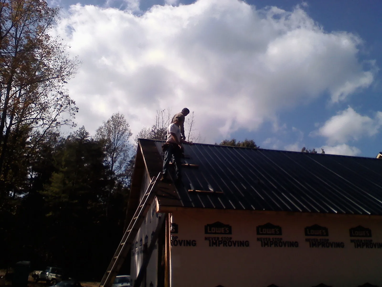 Roofer fastening dark metal panels high against a cloudy sky, from a Roof Inspection job in Verndale