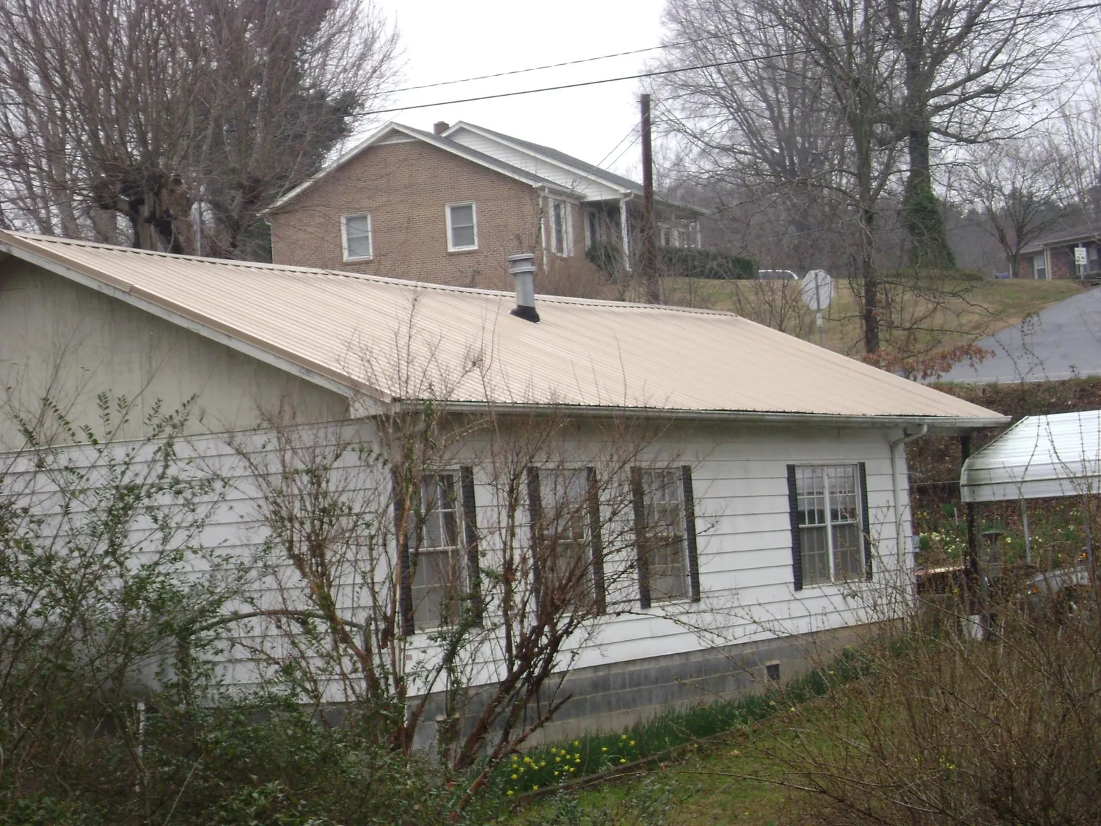 Tan metal roof on a white sided house set into a hillside — Commercial Roofing by Roofing Brothers in Verndale