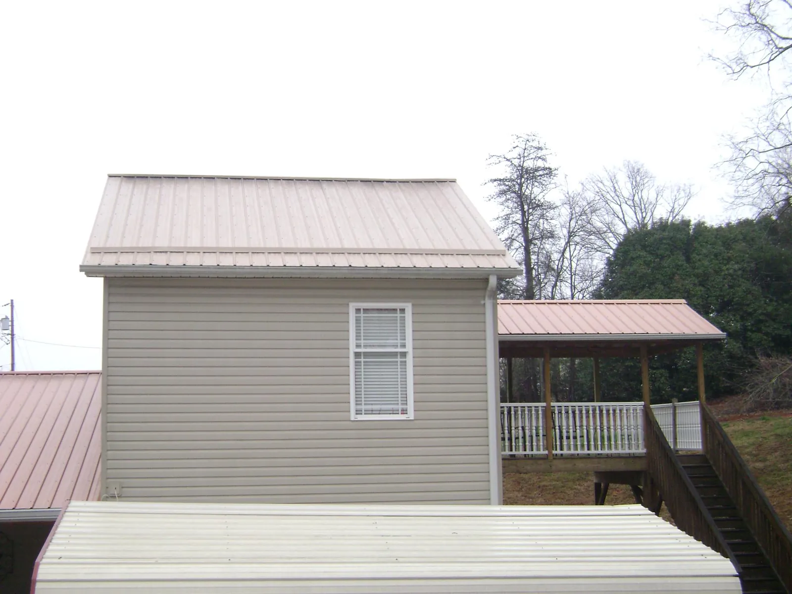 Tan metal roofs on a two story addition and attached porch, from a Roof Replacement job in Verndale