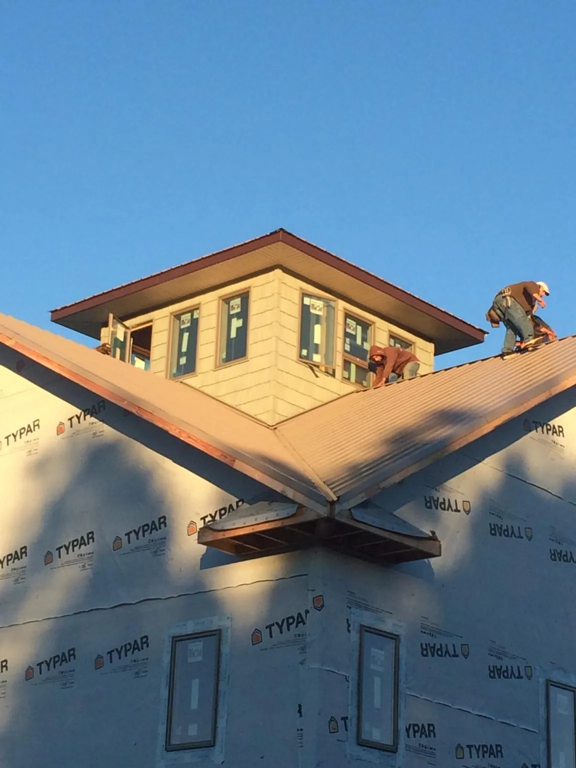 Roofers working around a rooftop cupola on a new metal roof at sunset — Roof Waterproofing in Verndale by Roofing Brothers